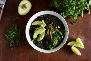 Black bean soup in a bowl with ingredients scattered around.