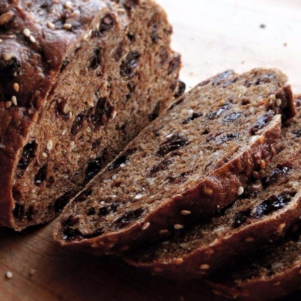 A close up of a loaf of pumpernickel raisin bread where it is sliced. Raisins and sesame seeds are visible.