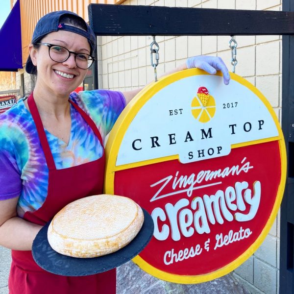 A Creamery staffer holding a wheel of Sunny Ridge cheese in front of the Cream Top Shop sign