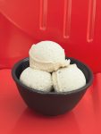 three scoops of bourbon gelato in a black bowl in front of a red background