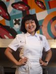 Chef Ji Hye Kim in a white apron in front of a painting in her restaurant