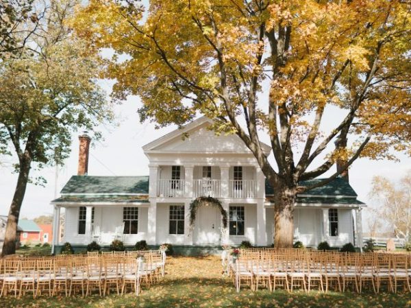 Exterior of Cornman Farms' white farmhouse in the fall with chairs set up