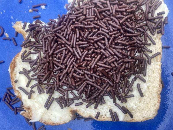 a piece of white bread spread with butter and covered with chocolate sprinkles on a blue plate