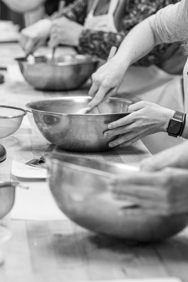 a black and white photo of people mixing something in large metal bowls